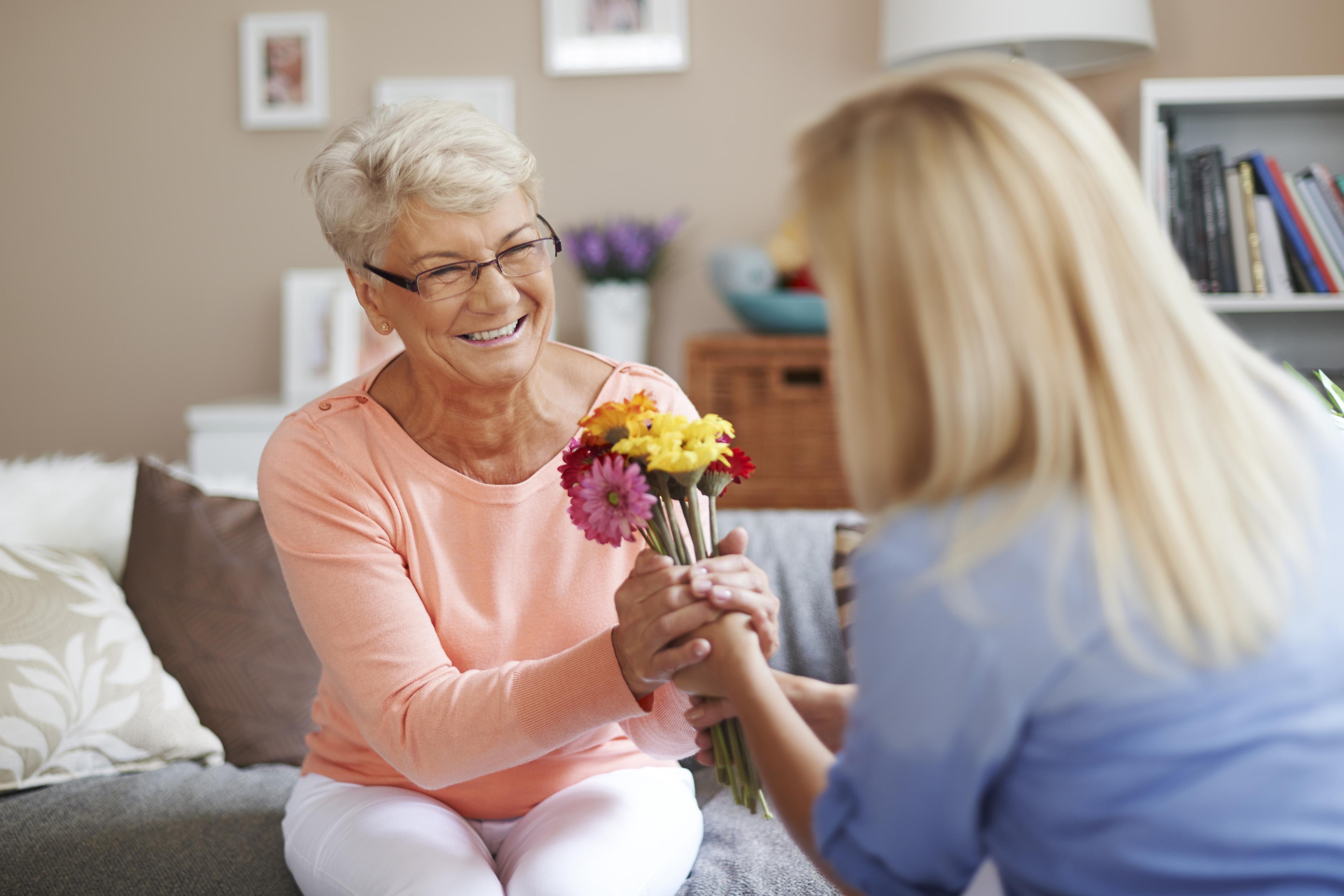 An old woman recieving flowers from a young female nurse.